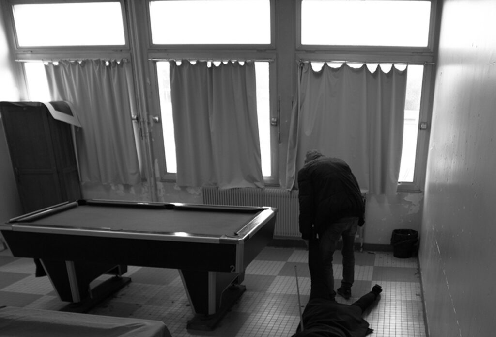 Salle de classe avec un billard retourné et un tissu au sol, scène sombre reconstituée pour le faux documentaire.
