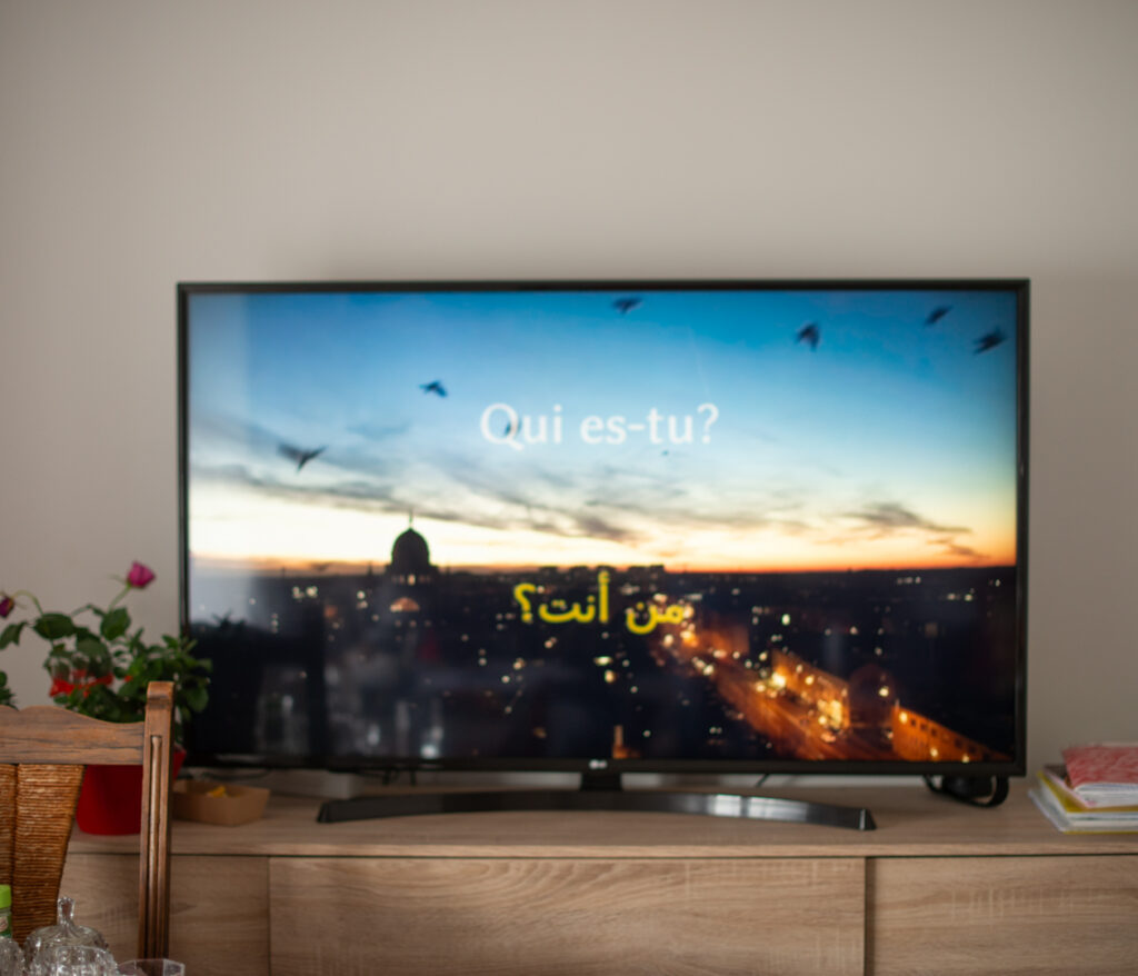 Écran de télévision affichant en arabe et en français la phrase « Qui es-tu ? »
