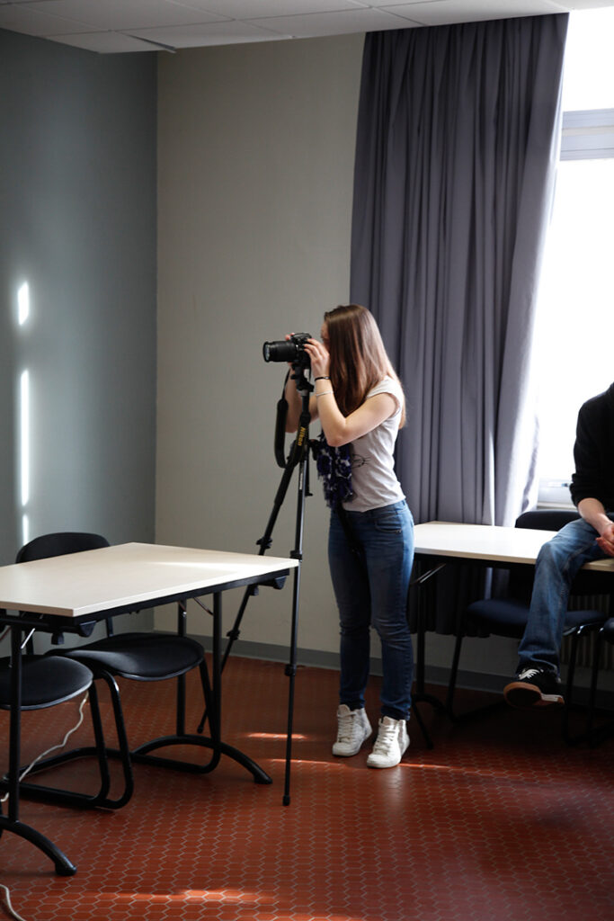 Personne debout tenant une caméra sur trépied dans une salle, atelier photo en situation de tournage.