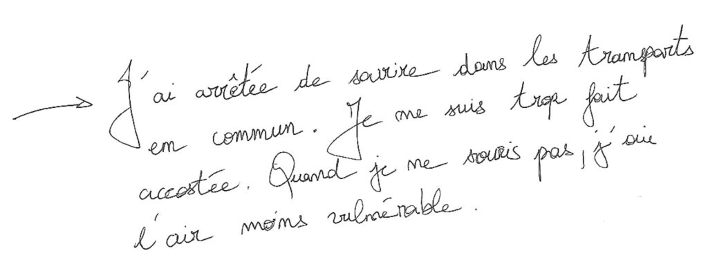 graffiti au stylo noir, une flèche au début indique qu'il répond à un autre graffiti, il est inscrit : J'ai arrêté de sourire dans les transports en commun. Je me suis trop fait accostée. Quand je ne souris pas, j'ai l'air moins vulnérable