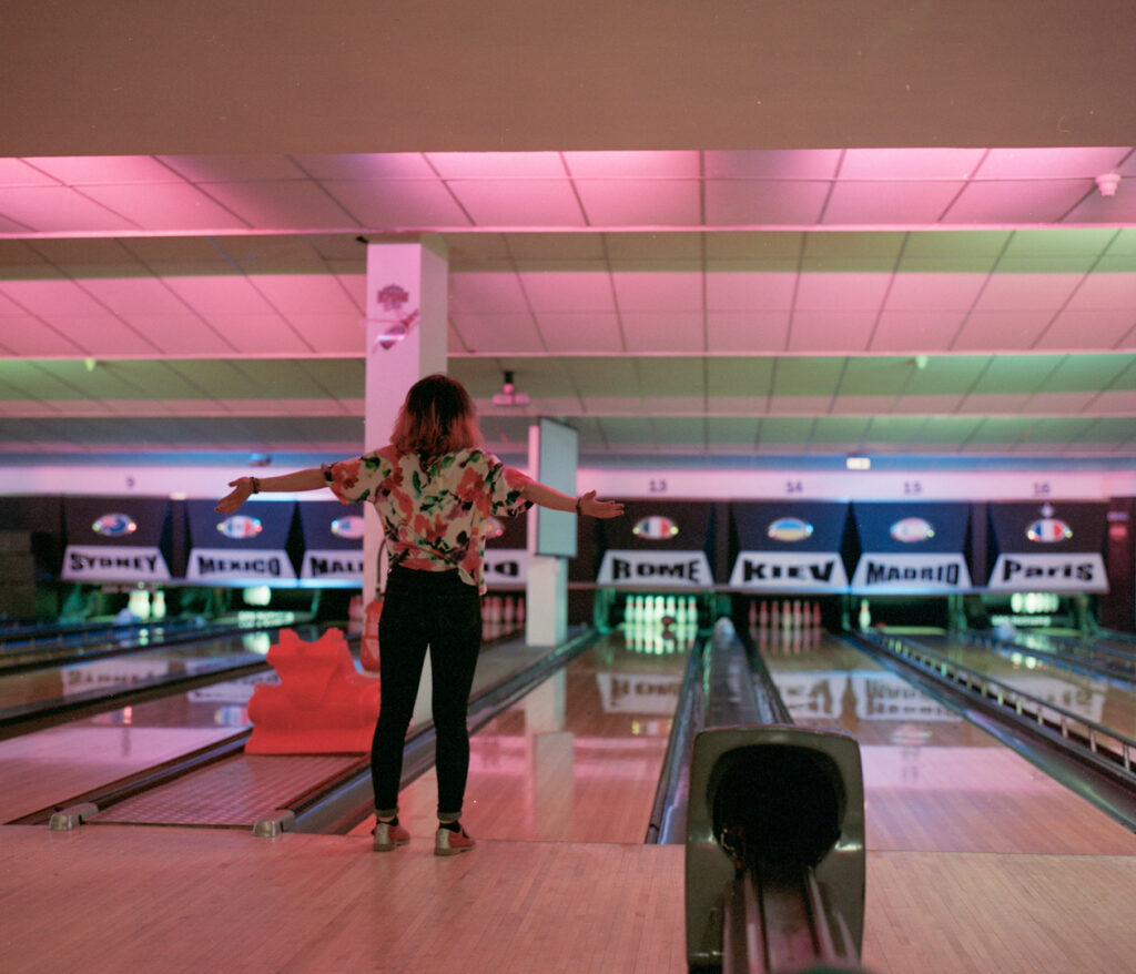 Yara joue au bowling ; au fond, les noms de plusieurs capitales sont visibles dans le décor